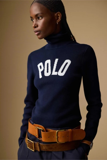 Fashionable Black woman in a Polo sweater and belts. Navy top with Polo logo, stylish belts, indoor studio shot.
