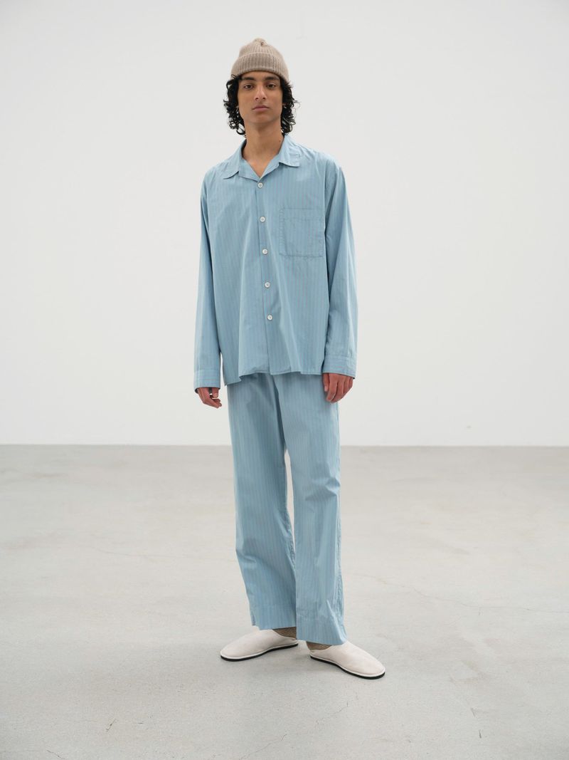 A person poses in a blue striped pajama set and a light brown beanie against a neutral background in a full studio shot.
