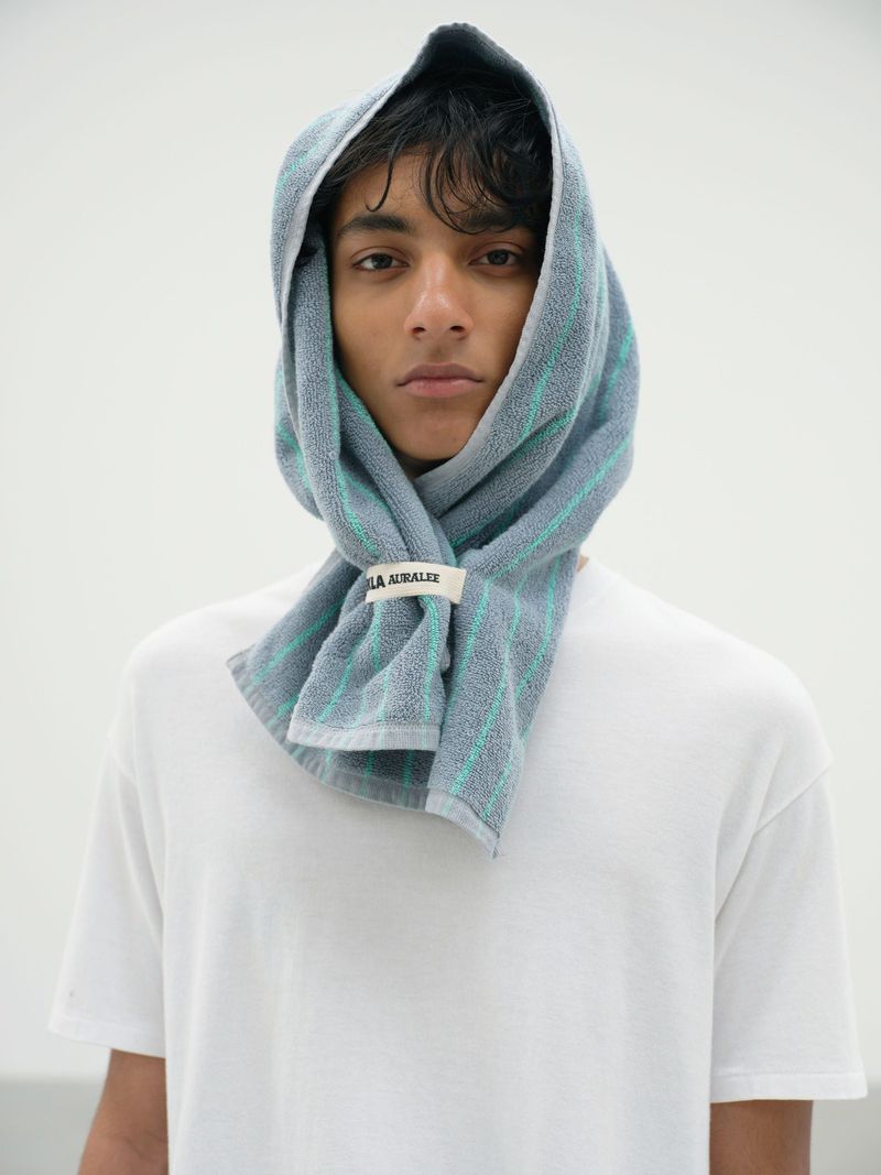 Portrait of a young adult male with gray striped towel wrapped around head and neck, wearing a white t-shirt against a white background.