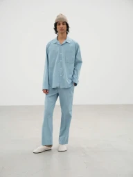 Model wearing a light blue button-down shirt and matching trousers with a beanie against a white seamless background
