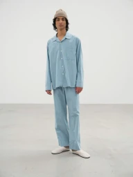 Model wearing a light blue striped pajama-style shirt and matching trousers with a beige beanie in a studio setting.