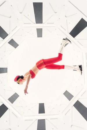 Woman in red outfit poses inside white geometric tunnel-like space, viewed from below, creating a sense of perspective and modern style.