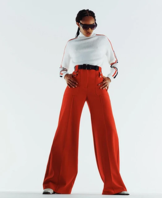 A fashionable woman poses in a white turtleneck with red accents and high-waisted, wide-legged red pants against a bright white backdrop.