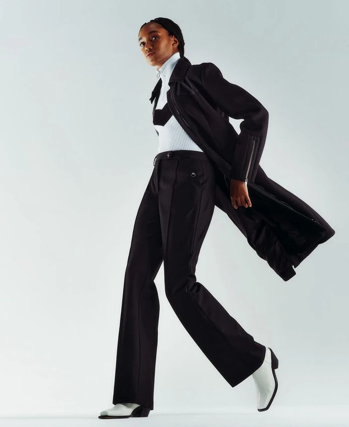 Model wearing a black coat and trousers with white boots against a clean white background