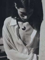 Model wearing a white button-down shirt and large pendant necklace in dramatic low-key lighting for Agmes