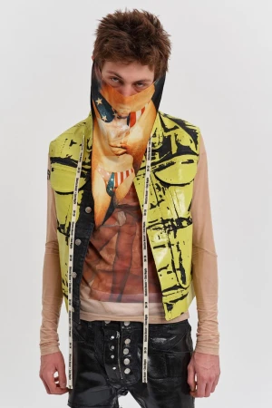 A person wears a graphic-print vest and a graphic-print face covering, standing in a bright studio against a white backdrop.