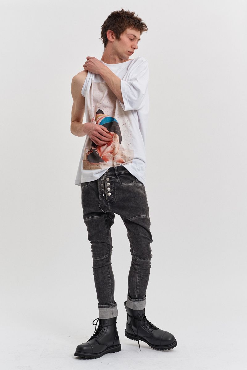 Full shot of a young adult man posing in a white tee shirt, acid-wash jeans with button details, and black boots on a white background.