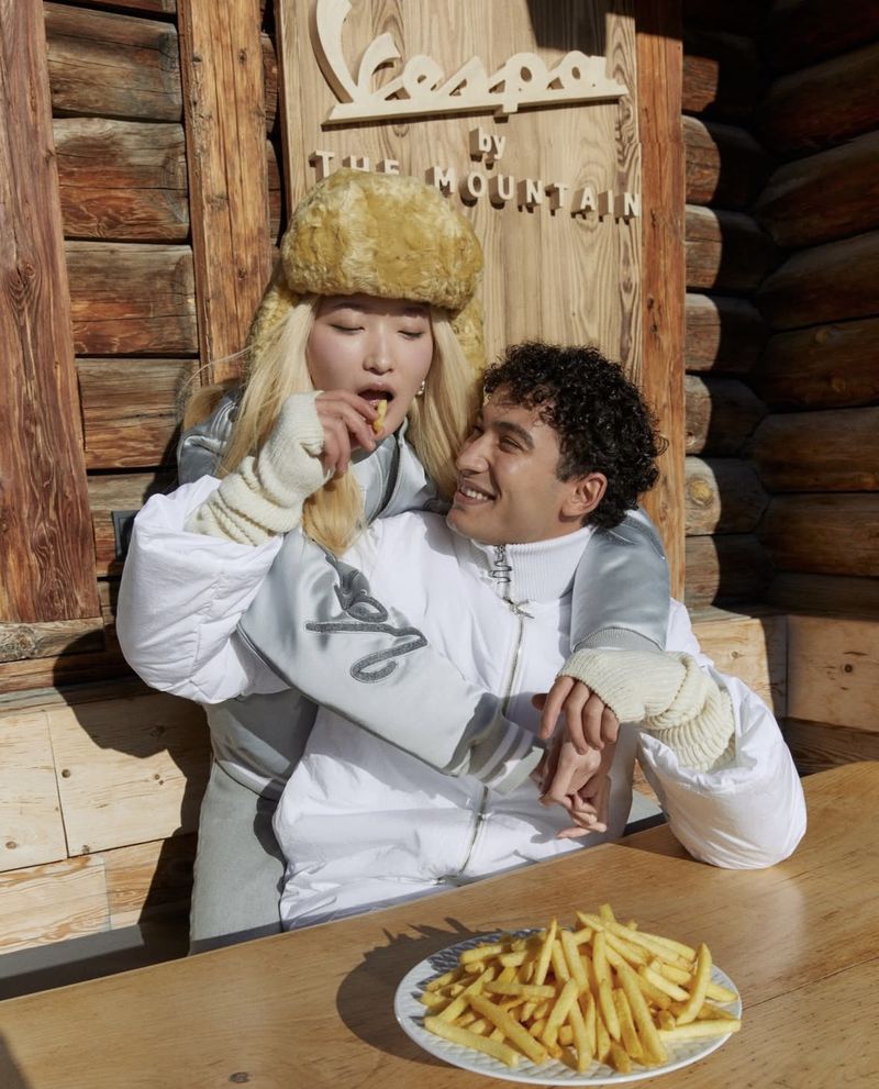 Two people share french fries outdoors in winter clothing, with a wooden building in the background, and the Cespa by The Mountain logo above.