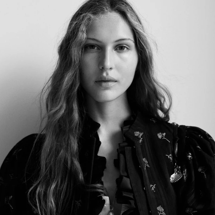 Portrait of a woman with long wavy hair wearing a black patterned blouse against a plain light background