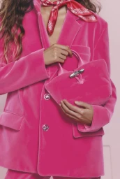 Model wearing a bright pink velvet blazer and neck scarf, holding a matching hot pink velvet handbag.
