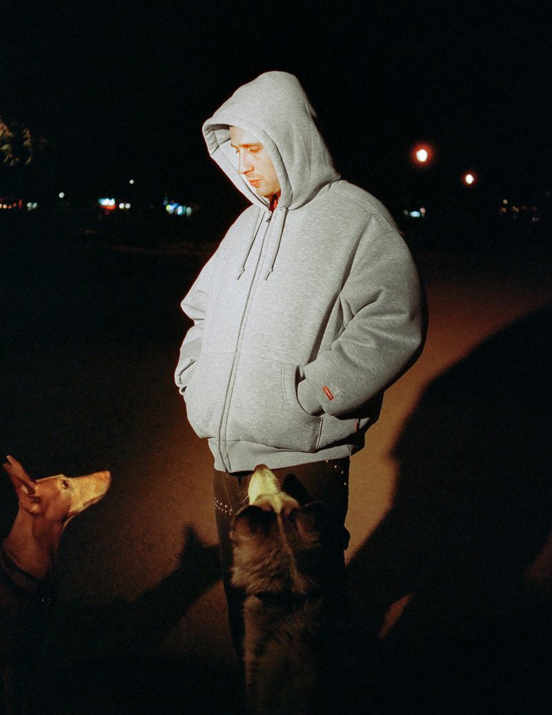 An adult male stands outside at night with two dogs; one is tan and short-haired while the other is a long-haired brown mutt.