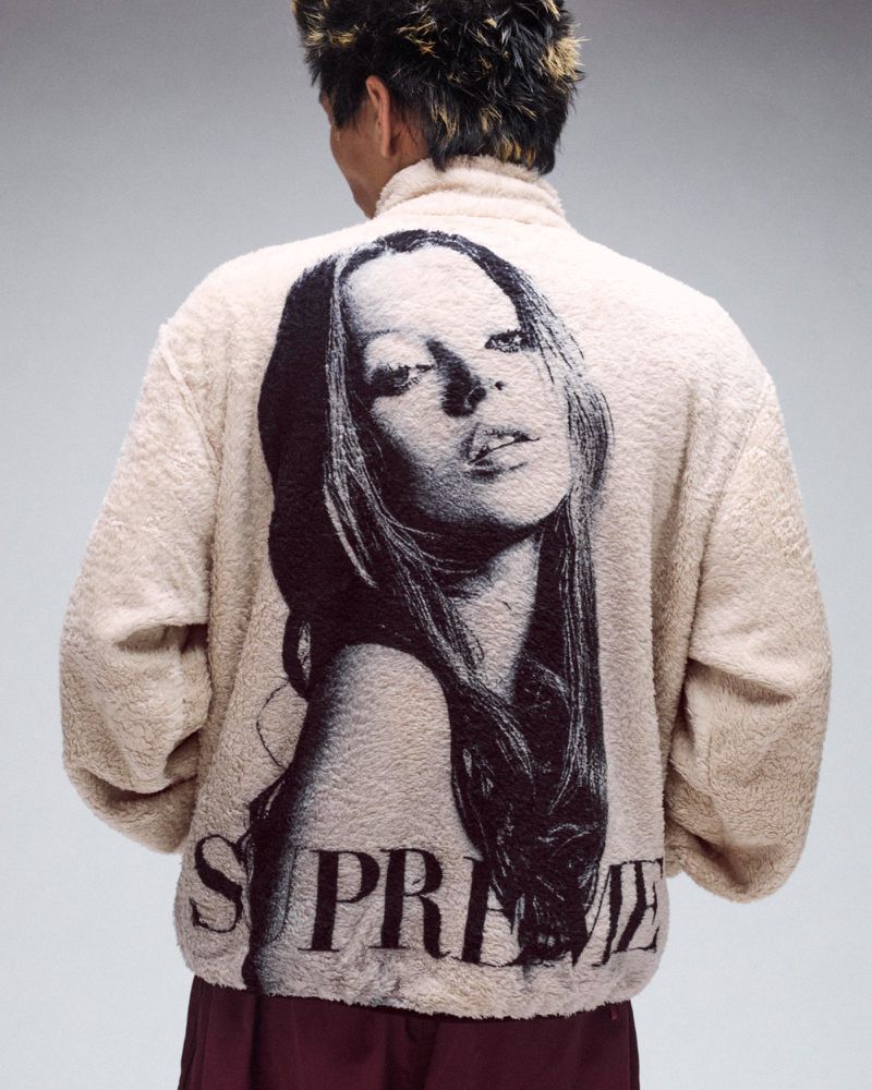 Person from the back wearing a cream-colored jacket with an illustration of a model, with the word 'Supreme' printed at the bottom.