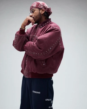 Man wearing a burgundy studded jacket and red bandana looking thoughtfully against a light grey background