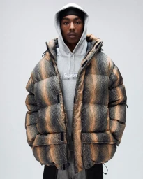 Man wearing a brown patterned puffer jacket over a grey hoodie and durag against a plain light grey background.