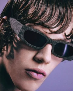 Close-up portrait of a model wearing dark-framed sunglasses with wet-look hair against a solid purple backdrop for Camper
