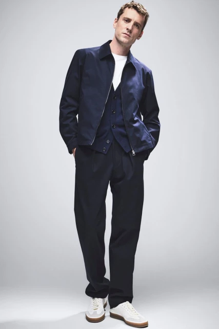 A man in a navy jacket and pants stands in a photo studio with neutral background, showcasing a modern, fashionable, and casual style.
