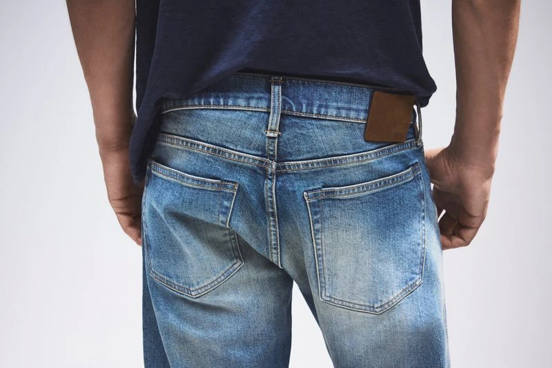 Rear view of a person wearing blue jeans and a dark blue t-shirt against a neutral background.  Fashion and style focus.