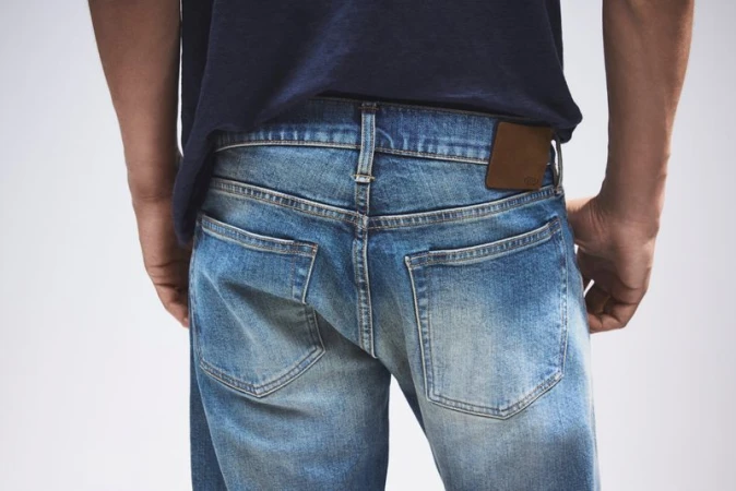 Rear view of a person wearing blue jeans and a dark blue t-shirt against a neutral background.  Fashion and style focus.