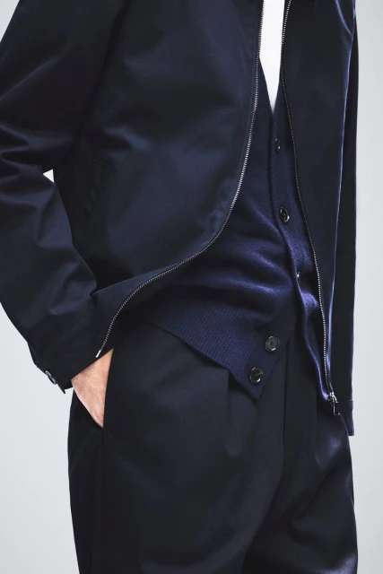 Close-up of an adult wearing a navy jacket, cardigan, and pants against a light background. Fashion and style are highlighted.