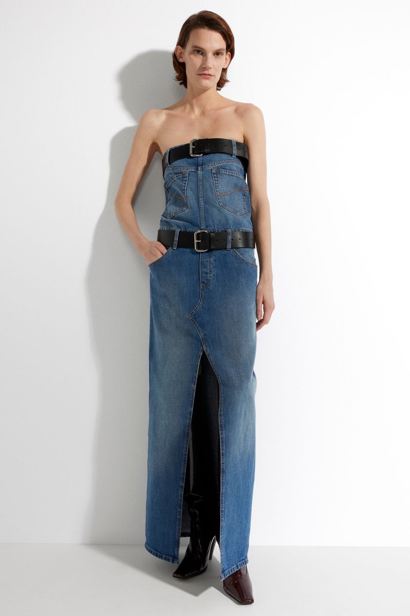 Woman in strapless denim dress with belts, full shot in a bright white studio.  Fashion editorial image with a modern, edgy aesthetic.