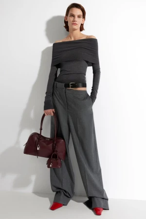 Fashion shot of a woman in a gray off-the-shoulder top and wide-leg pants, holding a burgundy satchel bag with matching miniature bag.