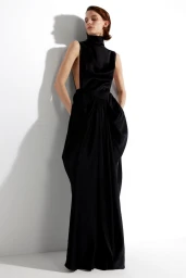 Model Lena Hardt wearing a black sleeveless dress leaning against a white studio wall casting a sharp shadow.
