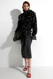Model wearing a black and grey patterned turtleneck sweater and skirt holding a handbag against a white background