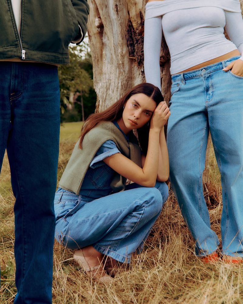 Model Candice Shepstone crouching in blue denim with a draped green sweater beside two standing models outdoors.