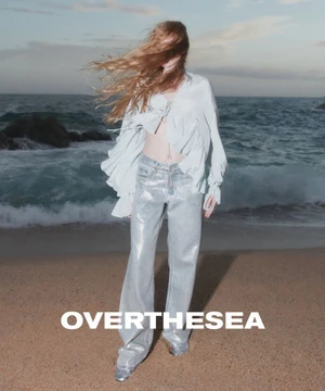 Model with blowing hair wearing a white ruffled blouse and metallic pants on a sandy beach