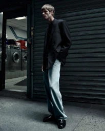 A man in a dark blazer and light trousers standing outside a storefront with a metal security shutter.