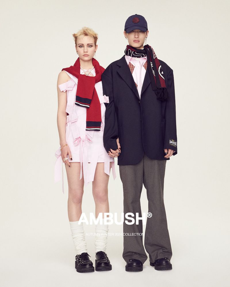 Two people in fashion forward outfits pose in a studio. A woman in a pink deconstructed dress and a man in an oversized blazer and hat.