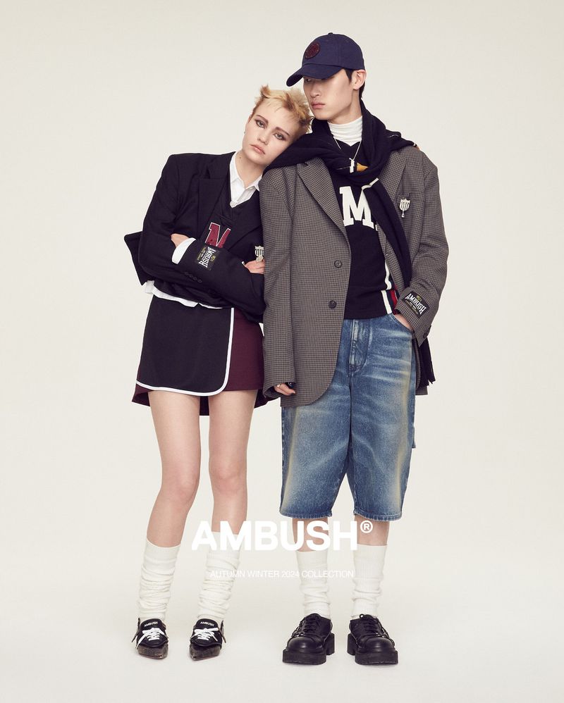 Two fashion models pose together in vintage-inspired outfits featuring a black blazer, skirt, denim shorts, socks, and black leather shoes.