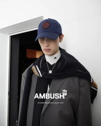 Model Jeong Junho in a navy cap, grey checked blazer, and draped black sweater for the Ambush Autumn Winter 2024 lookbook.