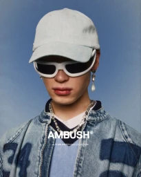 Model wearing a light denim cap, white futuristic sunglasses, and a denim jacket against a blue background