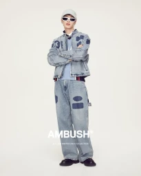 Model in a matching denim jacket and jeans wearing white sunglasses and a cap against a plain light background