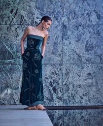 Dalton Dubois posing in a strapless dark teal embroidered velvet wide-leg jumpsuit against a large green marble wall.