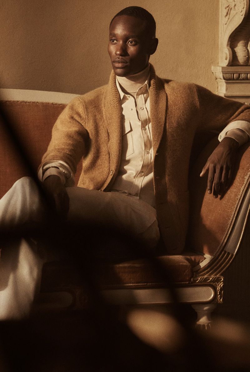 Portrait of an African American man in a cardigan posing on a chaise lounge indoors, with neutral tones and soft, warm lighting.
