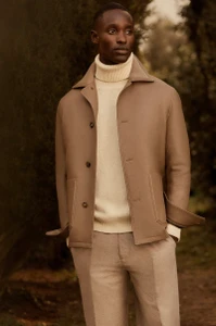 Model Charles Oduro wearing a camel jacket and cream turtleneck sweater outdoors for Brett Johnson FW25.