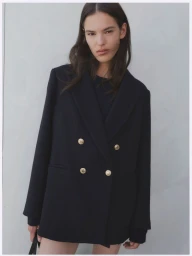 Model wearing an oversized black double-breasted blazer with gold buttons against a neutral grey studio background.