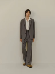 Model Luiz Silva wearing a tailored grey suit with wide-leg trousers and an open-collar white shirt against a neutral studio backdrop.