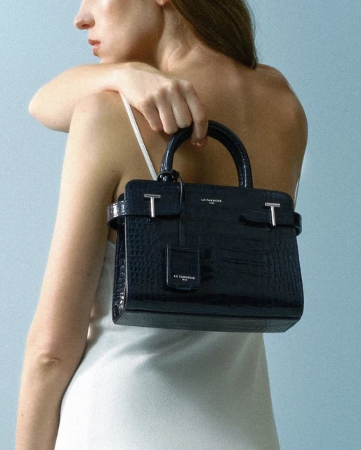 Elegant, crocodile-patterned handbag, held by a woman in a white dress against a light blue background, focusing on fashion and style.