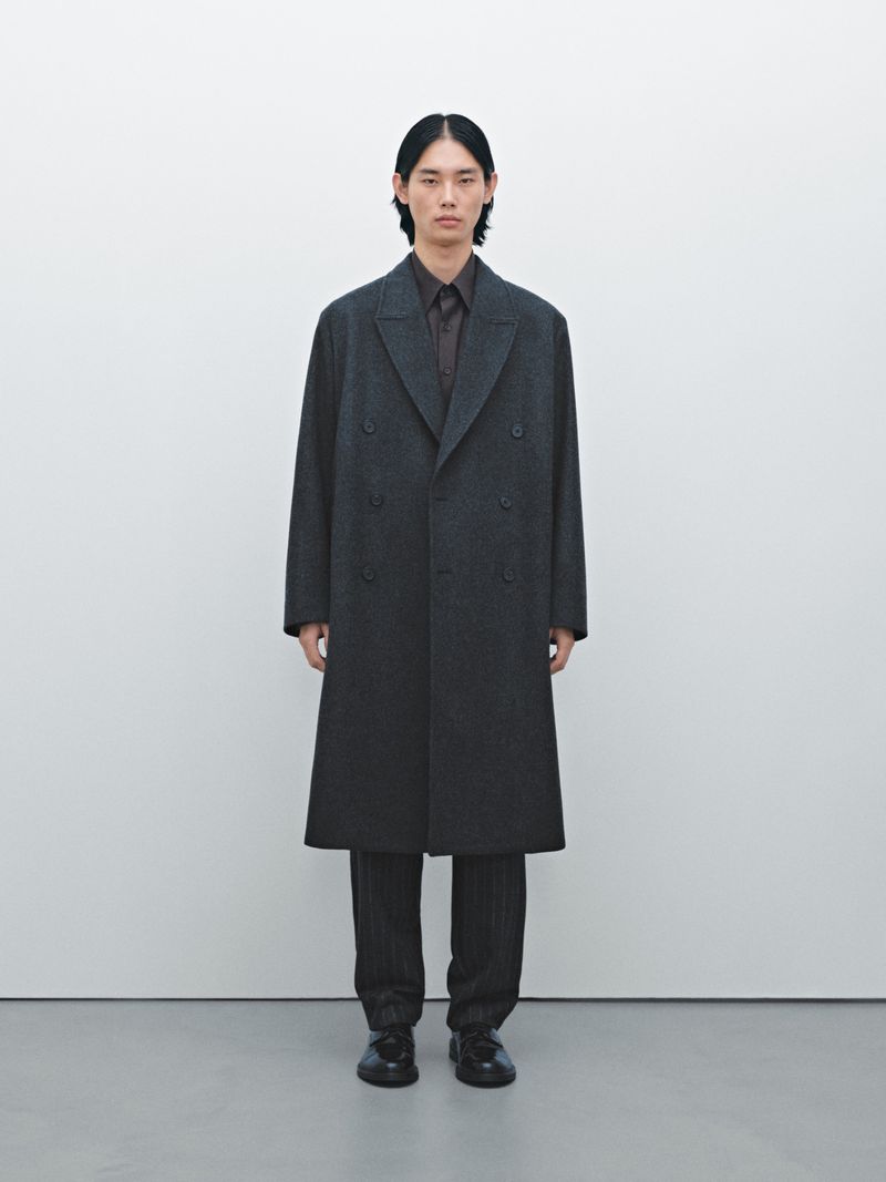 Model Taemin Park wearing an oversized dark charcoal overcoat and trousers against a clean white studio backdrop.
