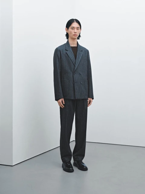 An Asian male model poses in a grey pinstripe suit indoors, standing against a white wall and grey floor with neutral lighting.