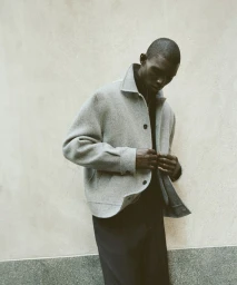 Model Fernando Cabral wearing a structured grey wool button-up jacket and dark trousers against a textured wall.