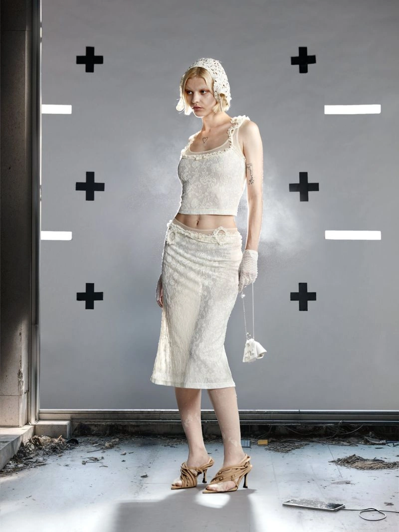 Model poses in a white lace crop top, midi skirt, and lace bonnet against a grey tracking marker backdrop.
