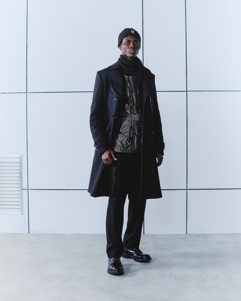 Adult male in a black overcoat, beanie and dress shoes in a white studio environment. Fashionable, elegant menswear attire.