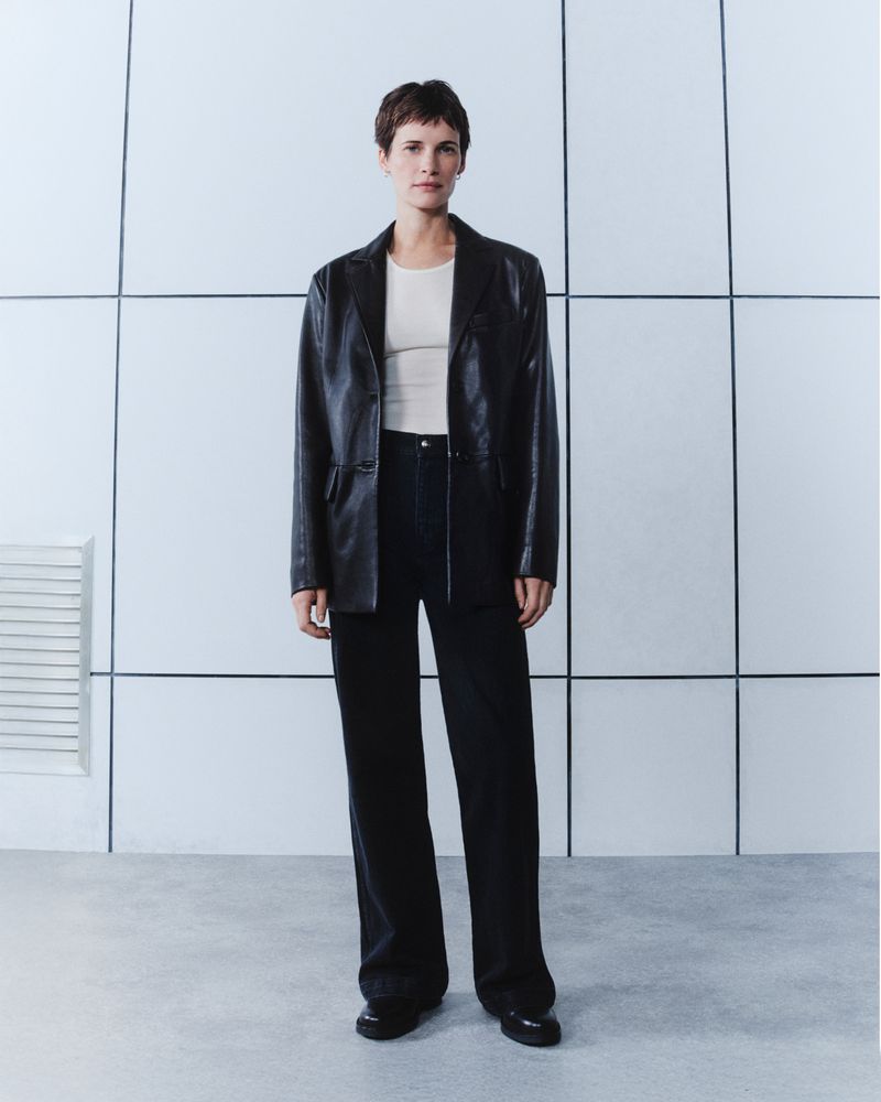 Model wearing a black leather jacket and dark trousers standing against a gridded wall for Belstaff AW/24