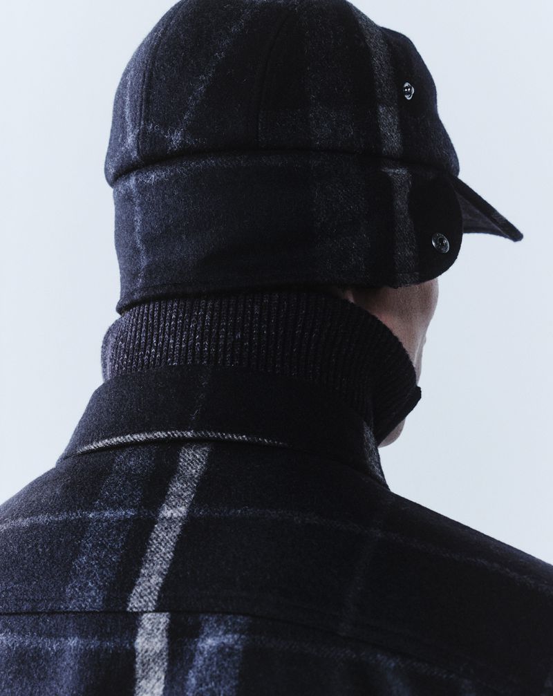 A person wearing a plaid cap and turtleneck is depicted from the rear, against a clean white backdrop.