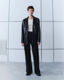 Model wearing a black leather jacket and dark trousers standing against a gridded wall for Belstaff AW/24
