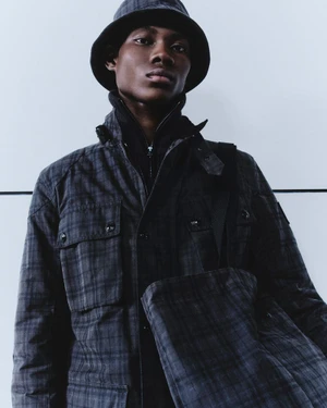 Model wearing a plaid jacket and matching bucket hat against a plain light wall background for Belstaff AW 24 lookbook.